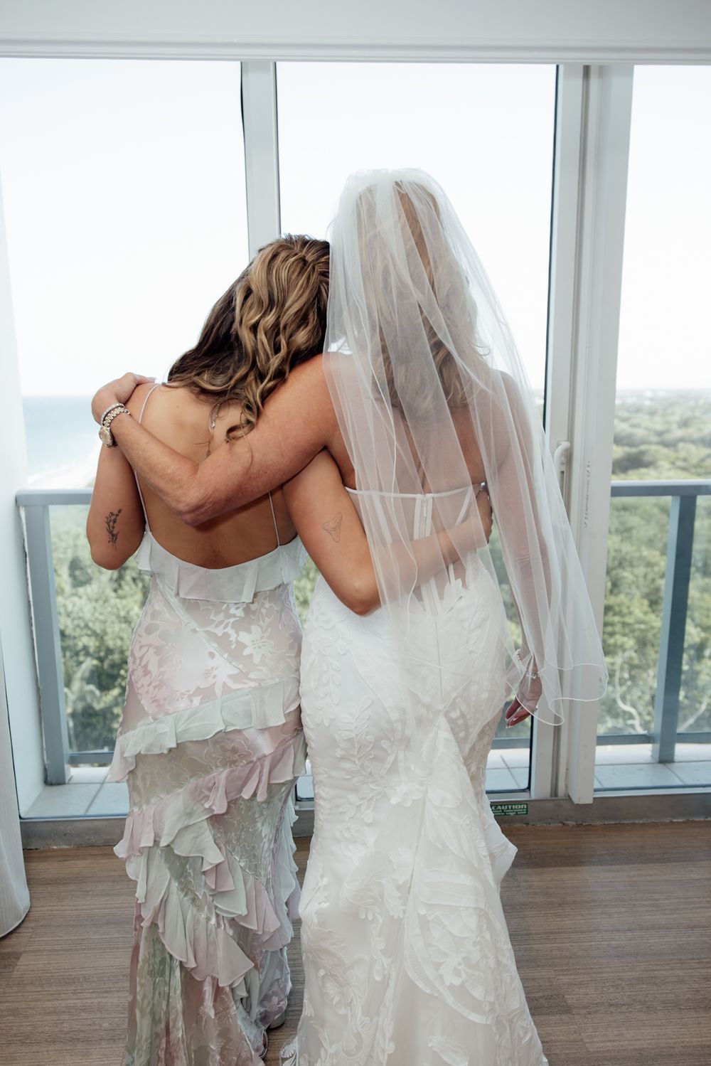 A row of bridesmaids in flowing white wedding dresses standing by a window with a scenic outdoor view.
