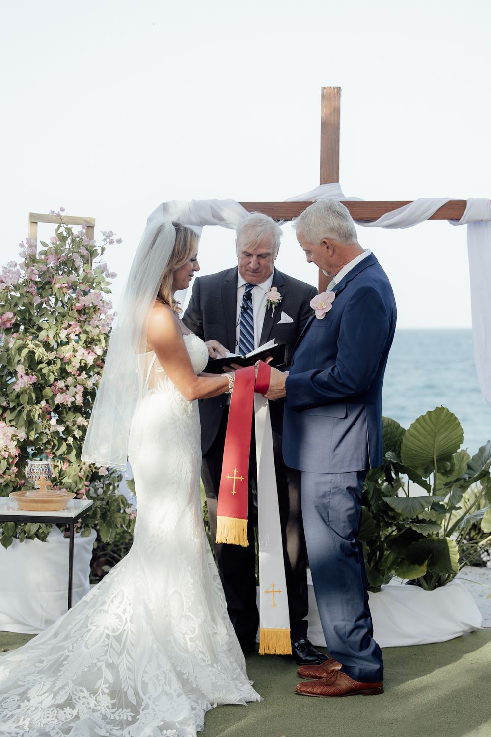Wedding ceremony taking place outdoors by the ocean with floral decorations.