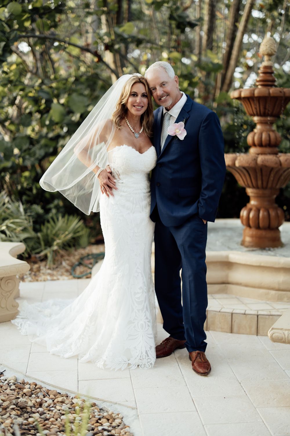 Wedding couple poses together outdoors in formal attire against a garden background.