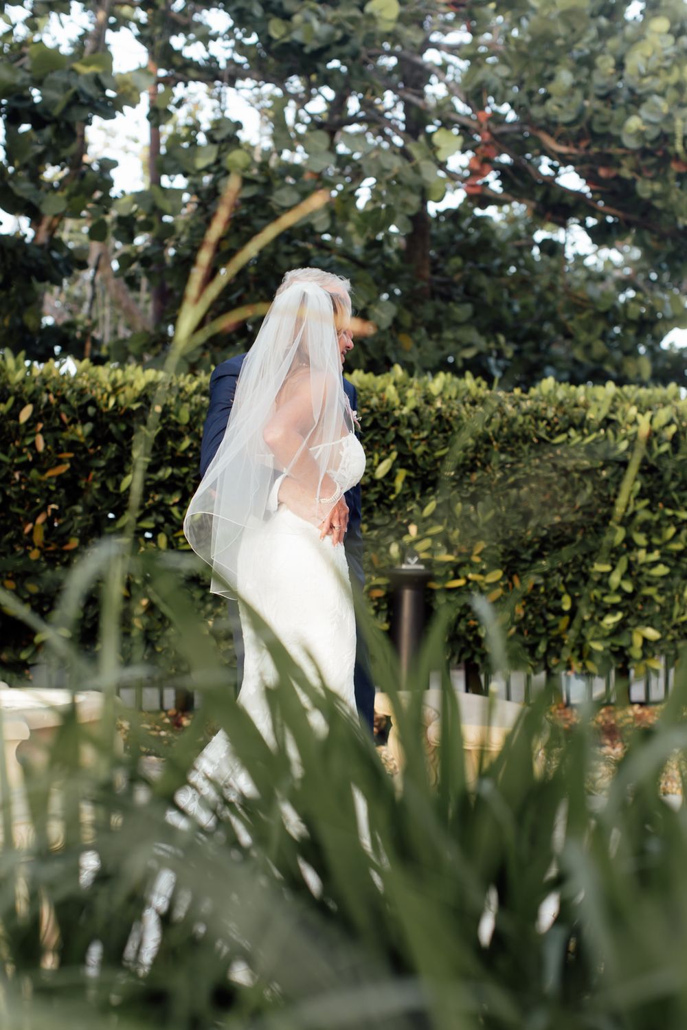 Elegant bride in white dress and veil standing in a lush garden setting.