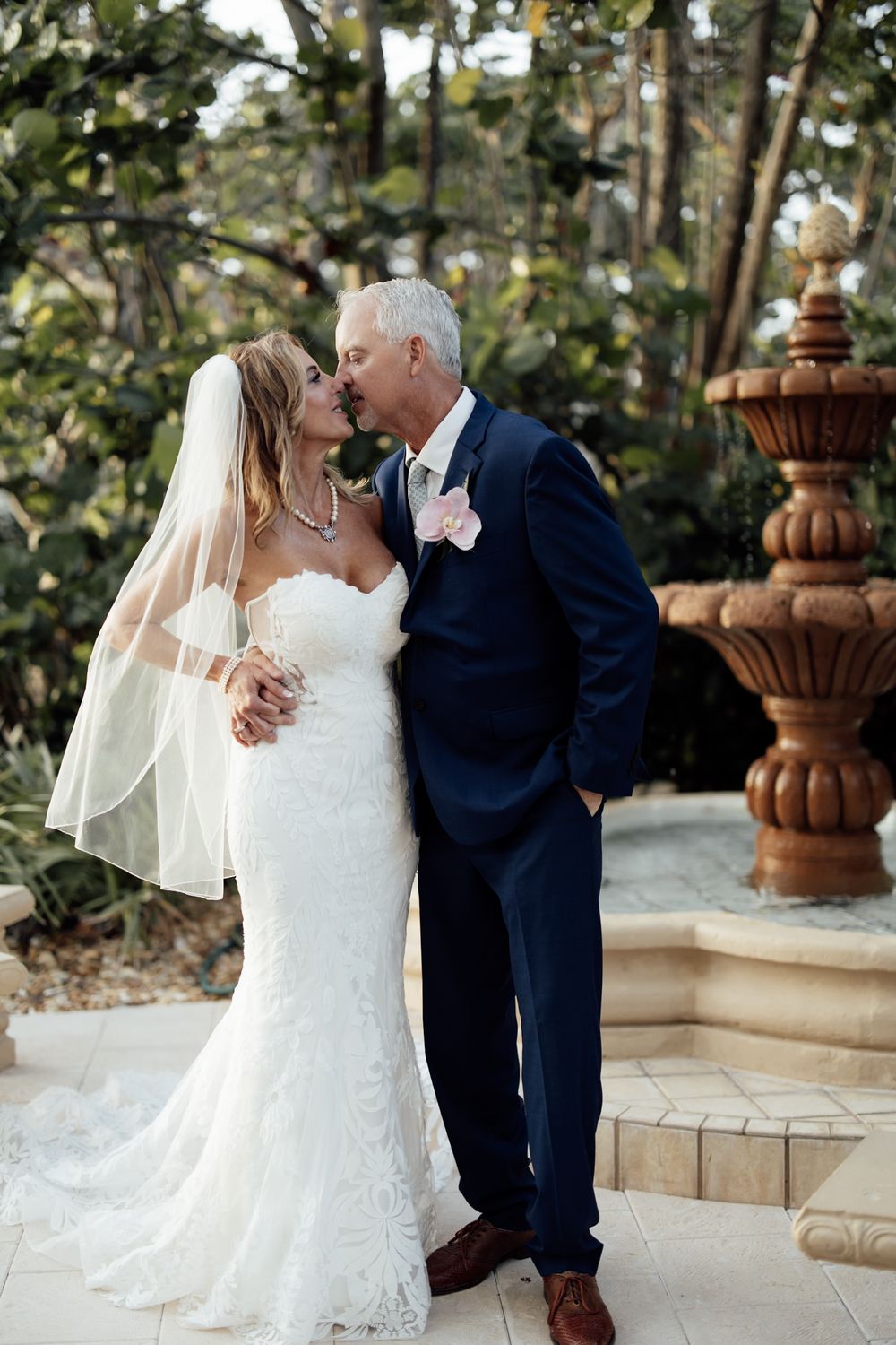 A couple shares a tender moment outdoors against a backdrop of garden architecture.