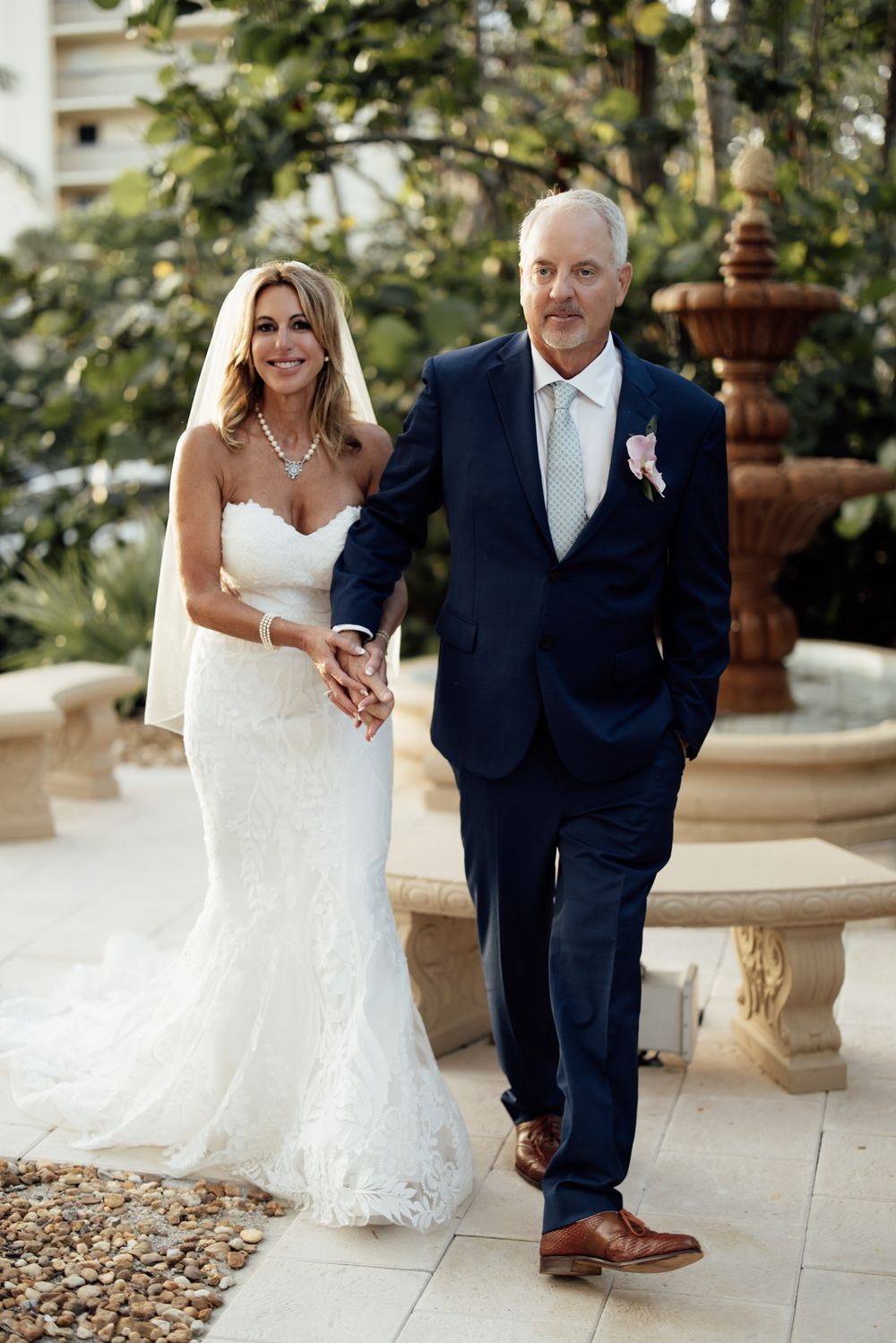 Wedding couple poses on a stone patio with tropical landscaping in the background.