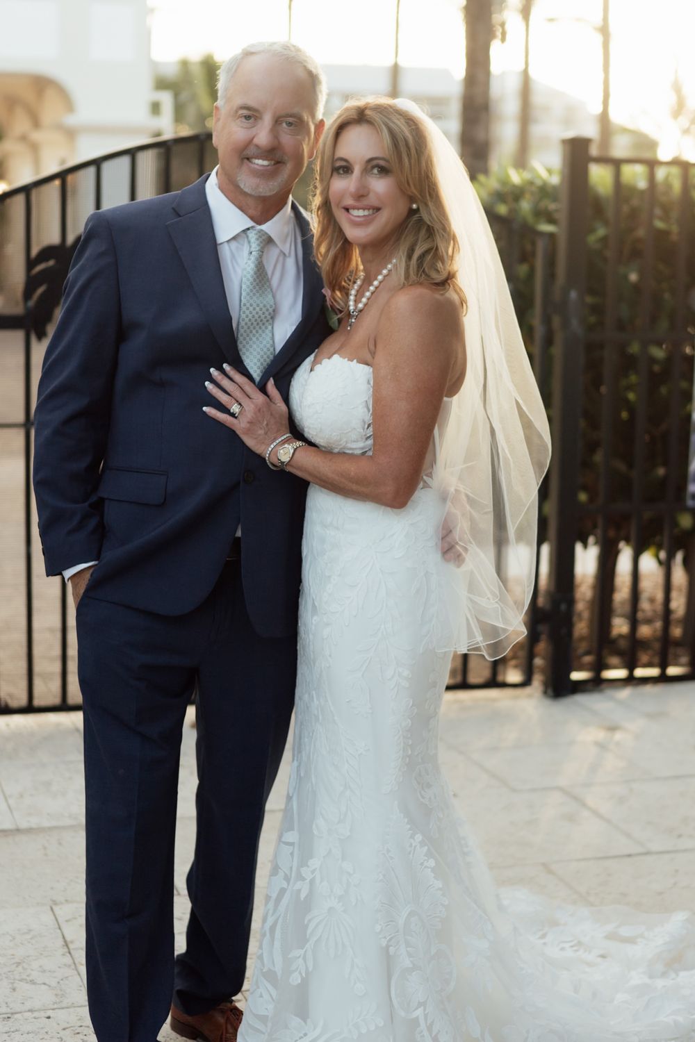 Elegant bride and groom pose for formal wedding portrait at sunset with palm trees in background.