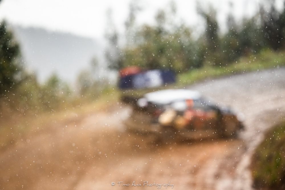 A car kicks up dirt and debris while racing on a dusty rally track during a competition event.