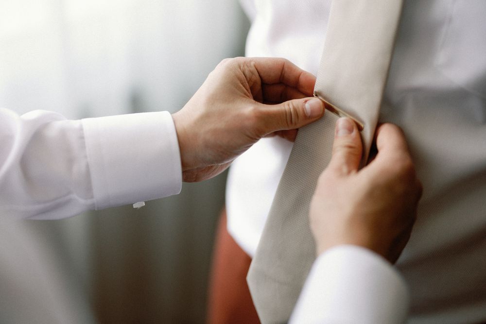Close-up of hands adjusting a white tie on a groom preparing for his wedding ceremony.