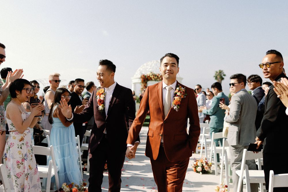 Newlywed couple walks hand-in-hand down the aisle as guests applaud at their outdoor wedding.