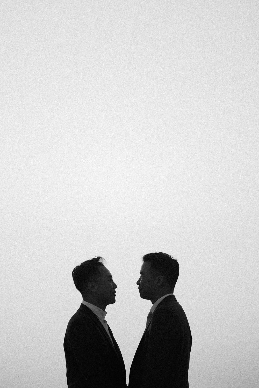 Black and white silhouette of two grooms facing each other in suits against a light background.