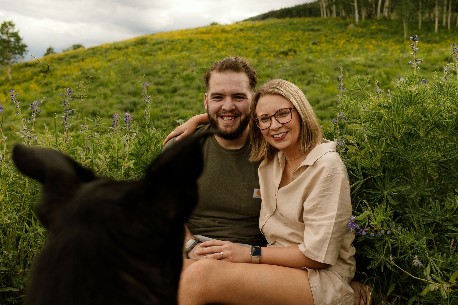 A couple embraces on a lush green hillside during a cloudy outdoor photo session.