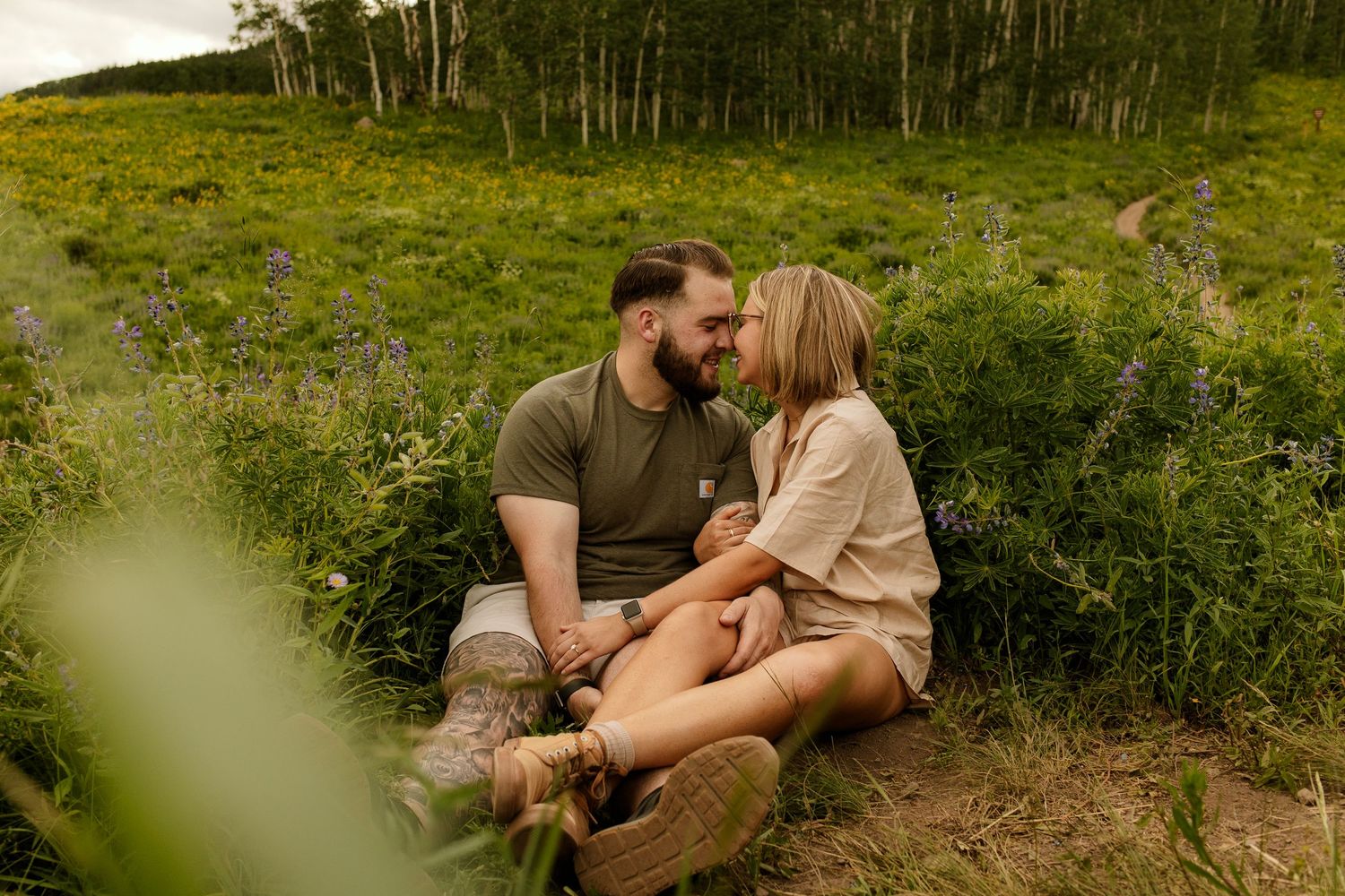 Couple enjoying a tender moment together while sitting outdoors in a lush green natural setting.
