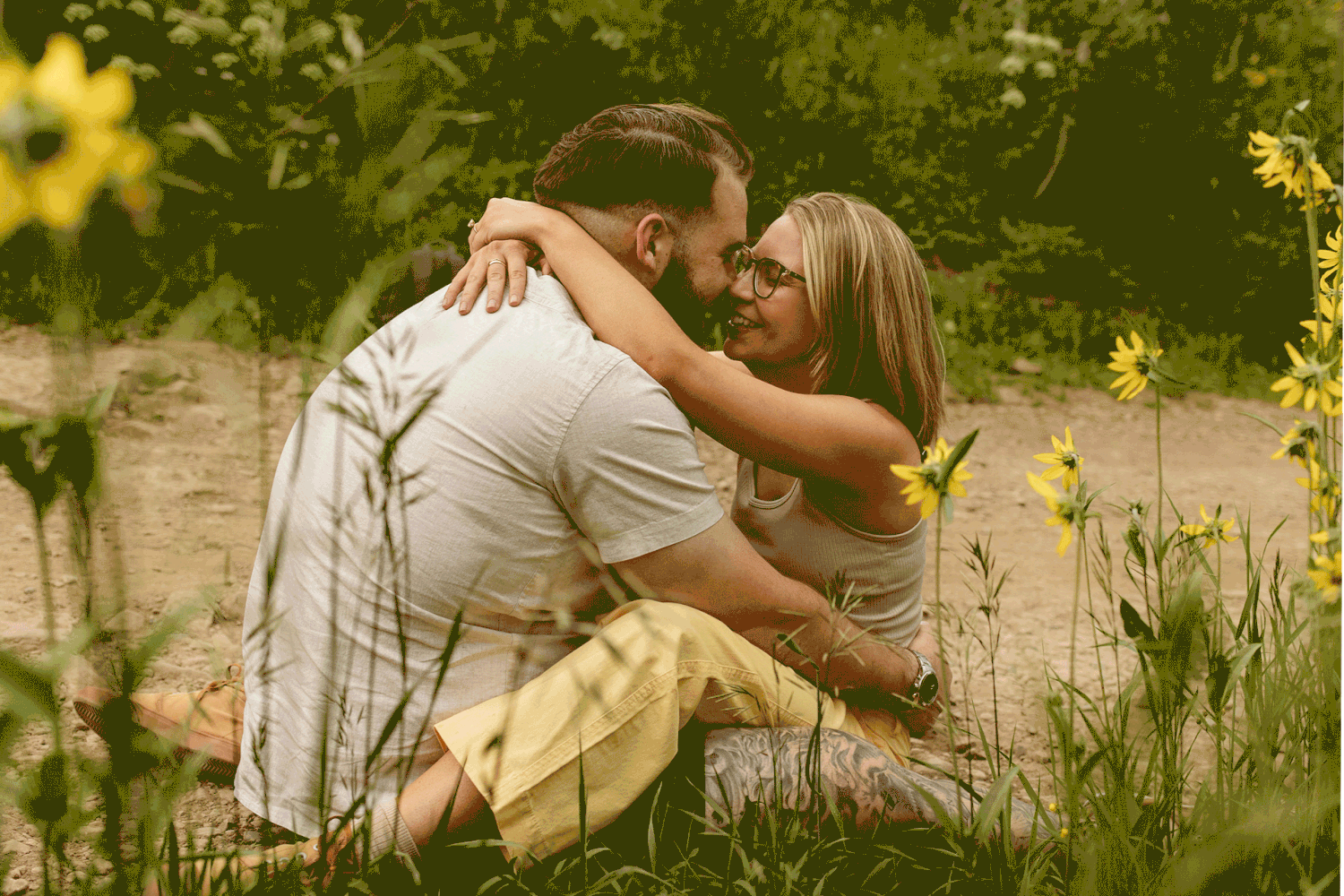 A couple embraces happily in a lush garden setting filled with sunlight and greenery.