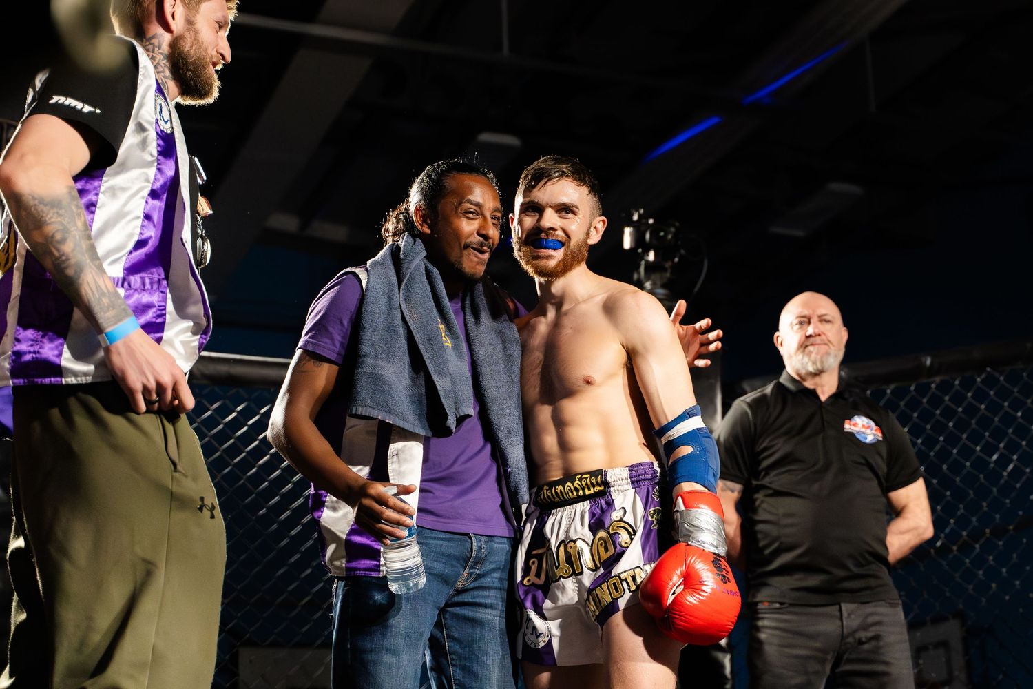 Combat sports athletes celebrating after a match in a dimly lit arena with purple lighting.