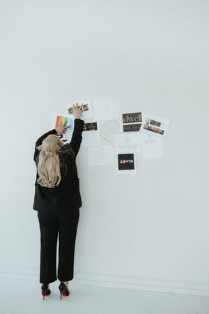 Person in black attire pinning photos to a white wall.