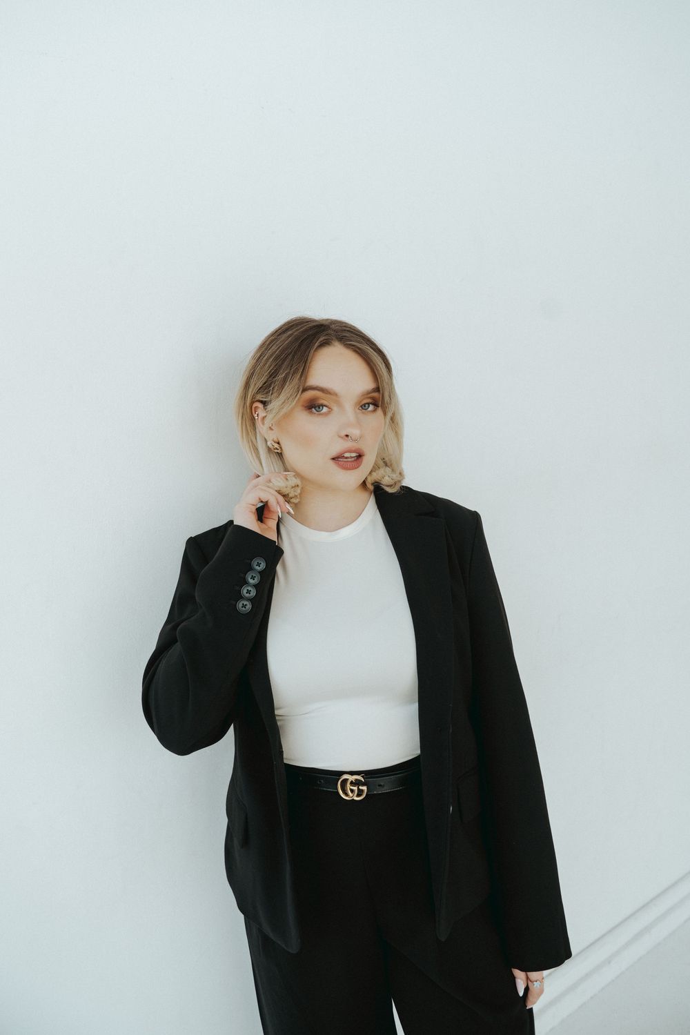 Stylish outfit featuring black blazer, white top and designer belt against white background.