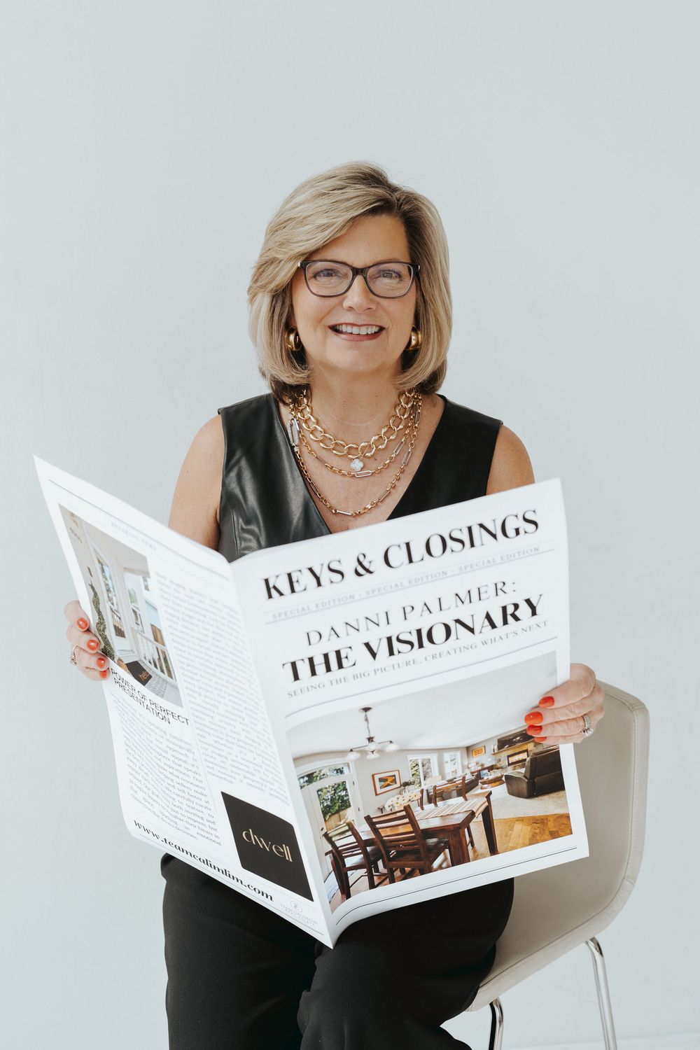 Business professional reading newspaper with glasses and black outfit against light background.