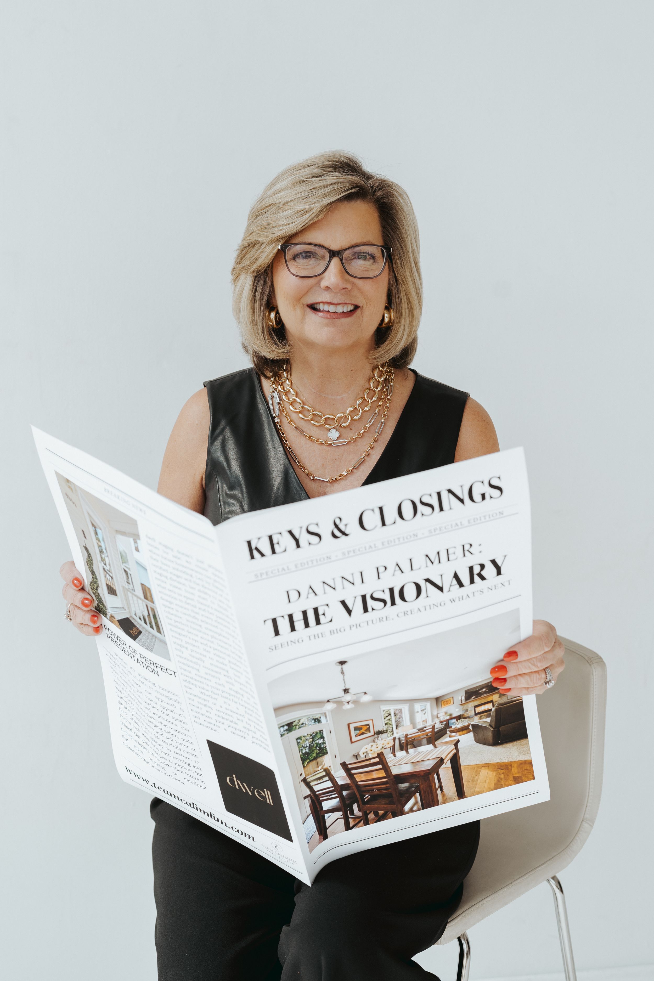 Business professional reading newspaper with glasses and black outfit against light background.