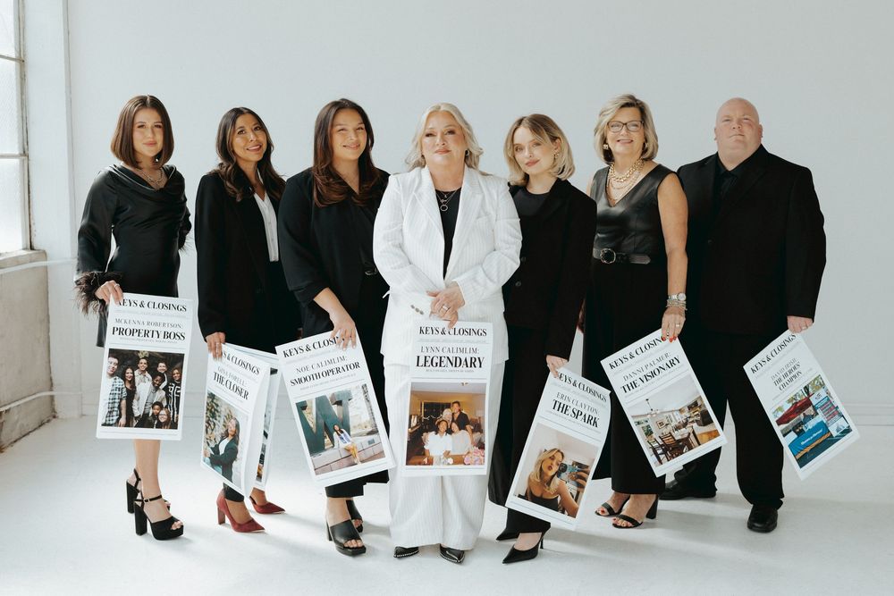 Group photo of real estate team in black and white outfits against light background.