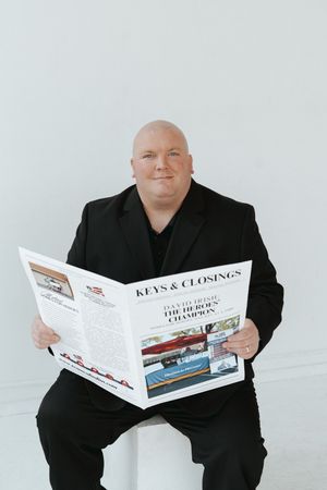 Two real estate professionals posing with Keys & Closings magazine against white backdrop.