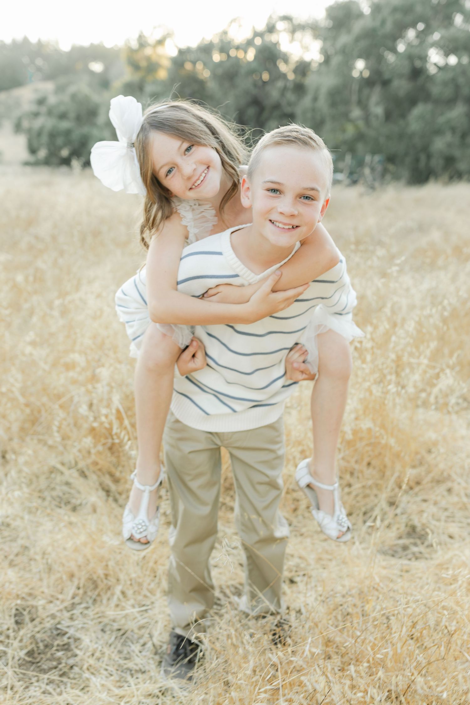 A joyful piggyback moment between two people captured in a golden field during sunset captured by Chelsee Rawe Photography.