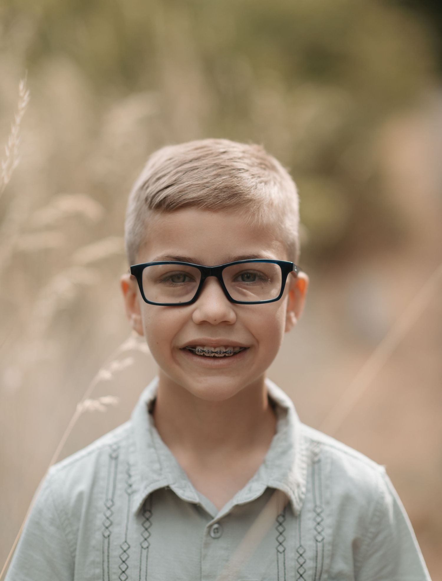A young boy smiling during a family photo session in Spokane, Washington. He stands outdoors with natural lighting, surrounded by fall color
