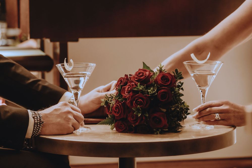 Close up of hands signing paperwork with a burgundy floral bouquet centerpiece on a wooden table.