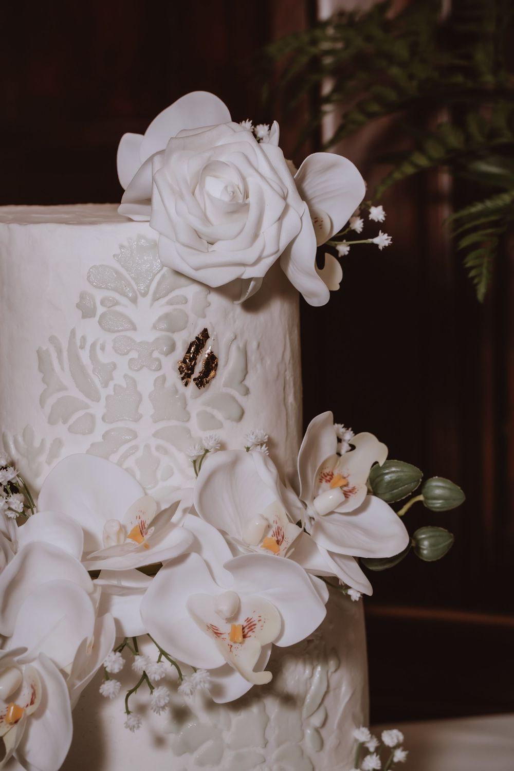 White orchids and roses adorn an elegant tiered wedding cake with delicate white floral patterns.