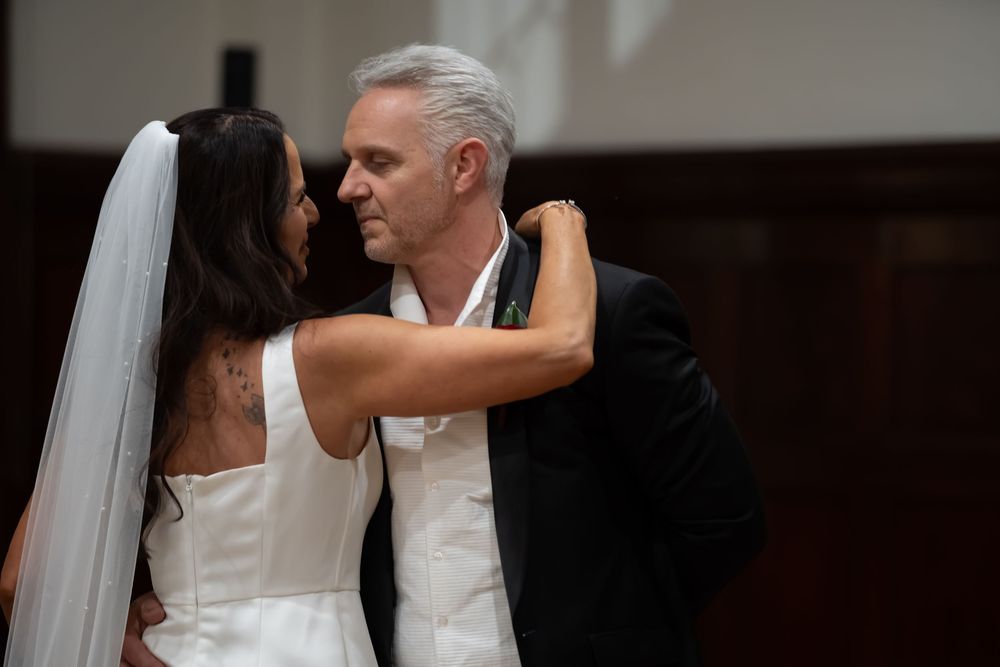 A bride and groom share an intimate dance during their wedding reception in a dimly lit ballroom.