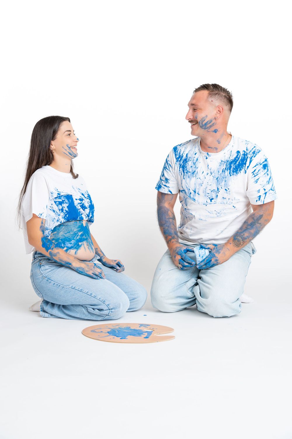 People in white t-shirts and jeans sit together on the floor with blue artistic paint splatter patterns.