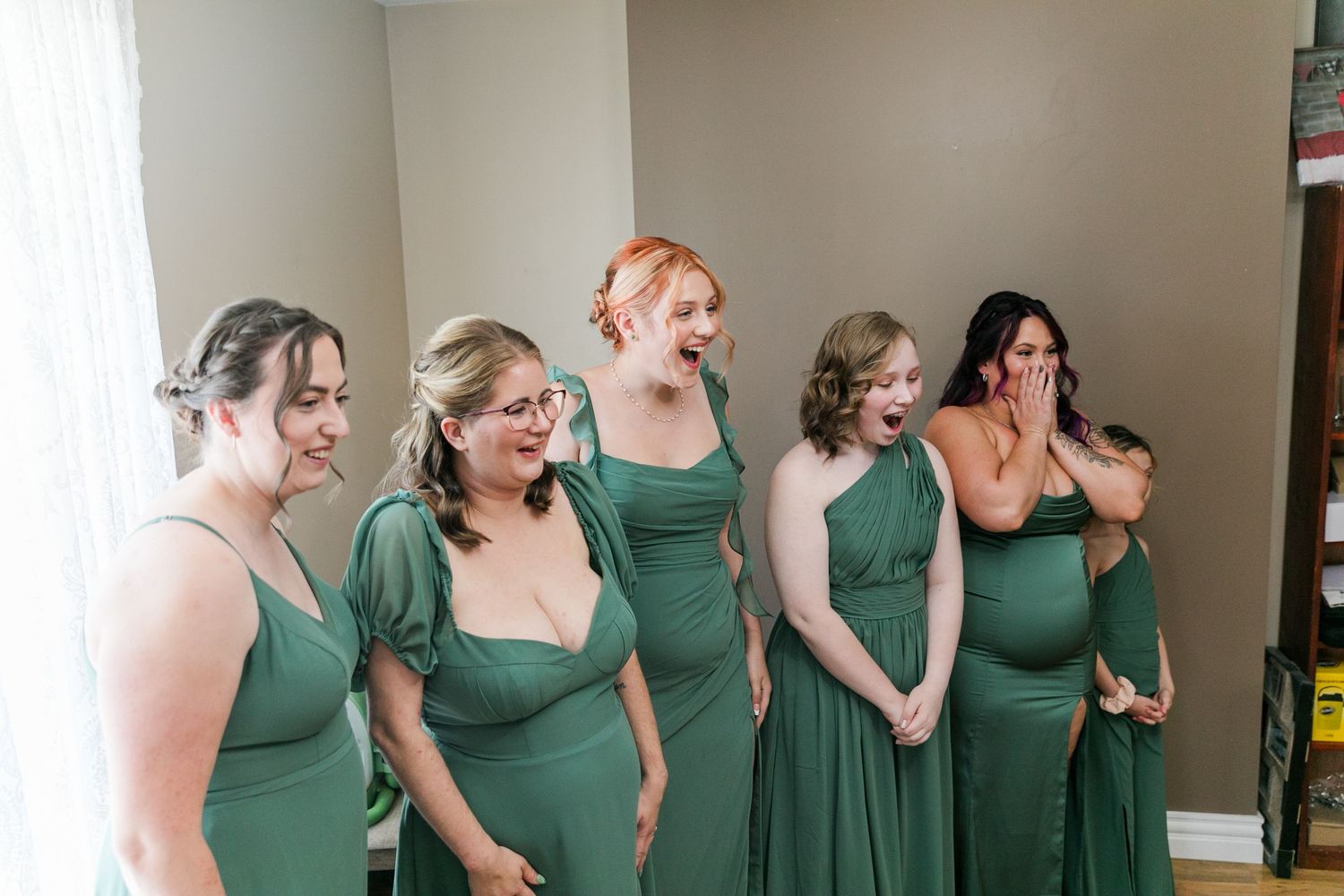 A group of bridesmaids share a candid moment while wearing emerald green dresses at a wedding.