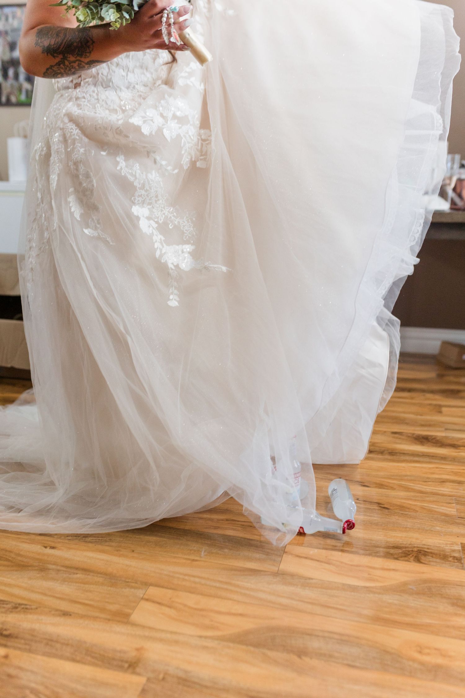 A flowing white wedding dress with delicate lace details sweeps across a hardwood floor, showing a glimpse of red shoes beneath.