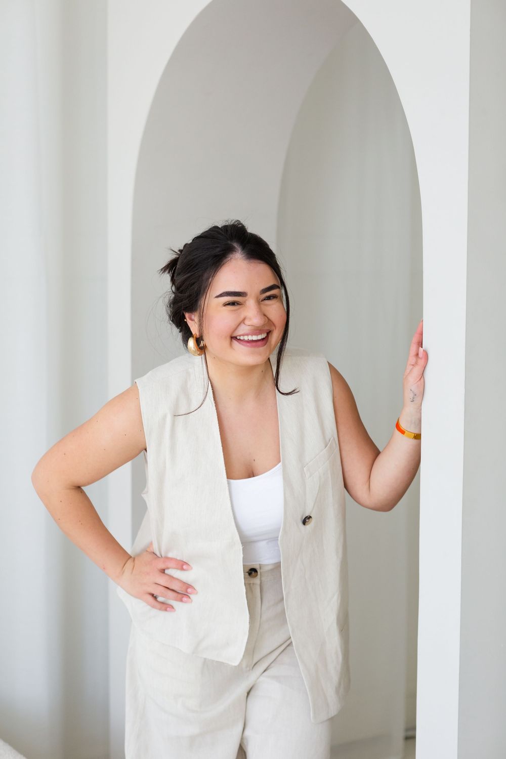 Happy person wearing a cream linen suit poses and laughs while standing in an arched doorway.