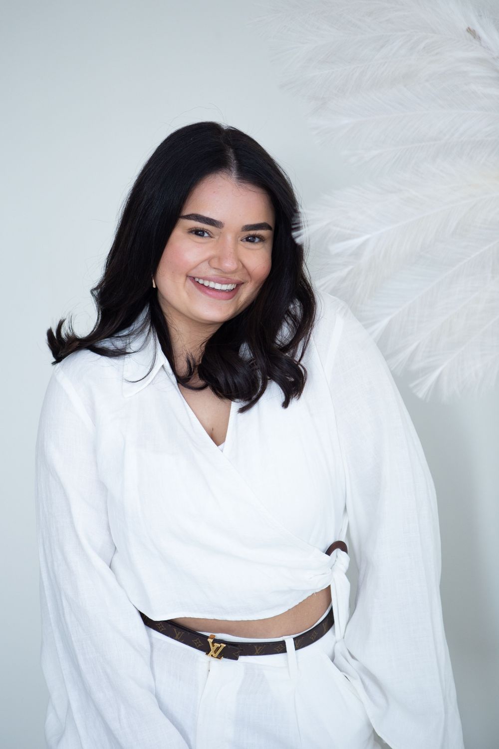 Person in white wrap style top and dark belt poses against light background with flowing white fabric.