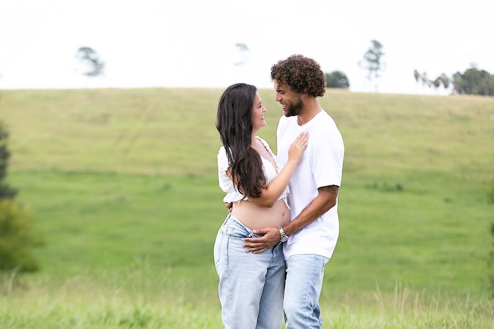 A couple embraces while standing in a green field. Orlando Maternity Photography, Sanford Maternity Photography, Outdoor Maternity Photos