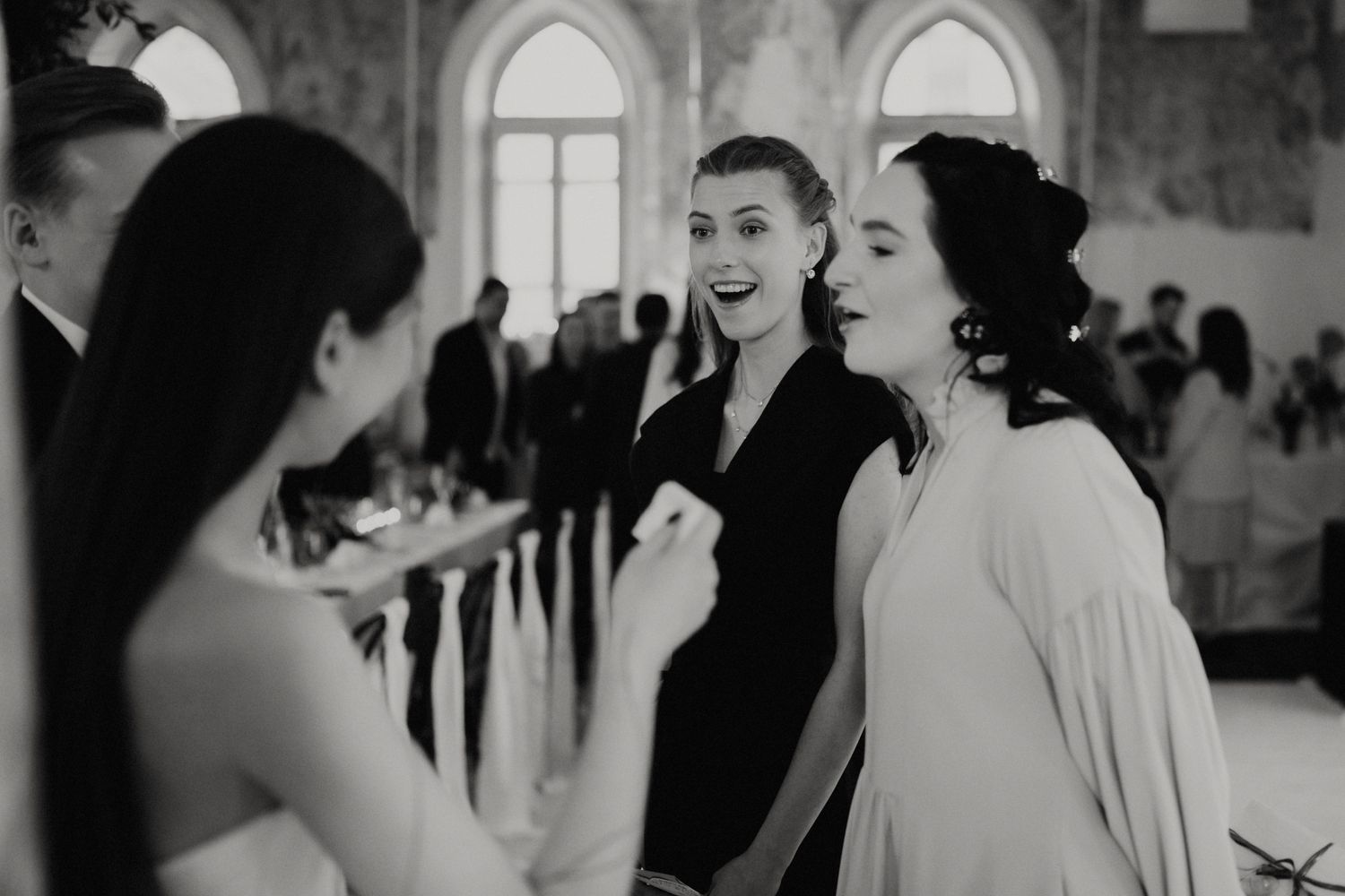 Wedding guests dancing and celebrating in an elegant venue with arched windows.