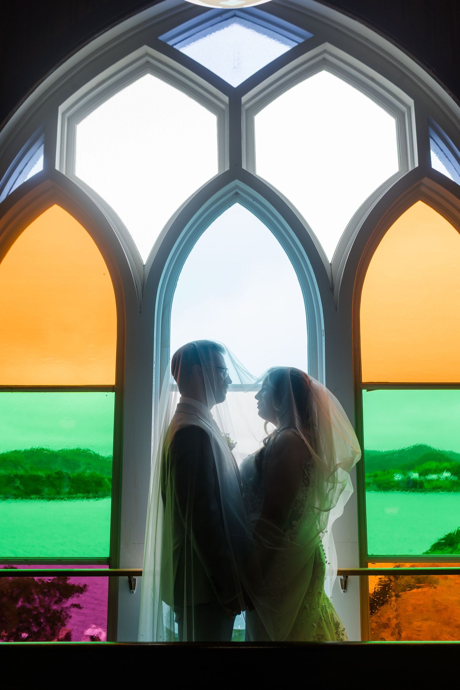 Silhouettes of people frame colorful views through gothic arched windows displaying a vibrant landscape in green and orange tones.
