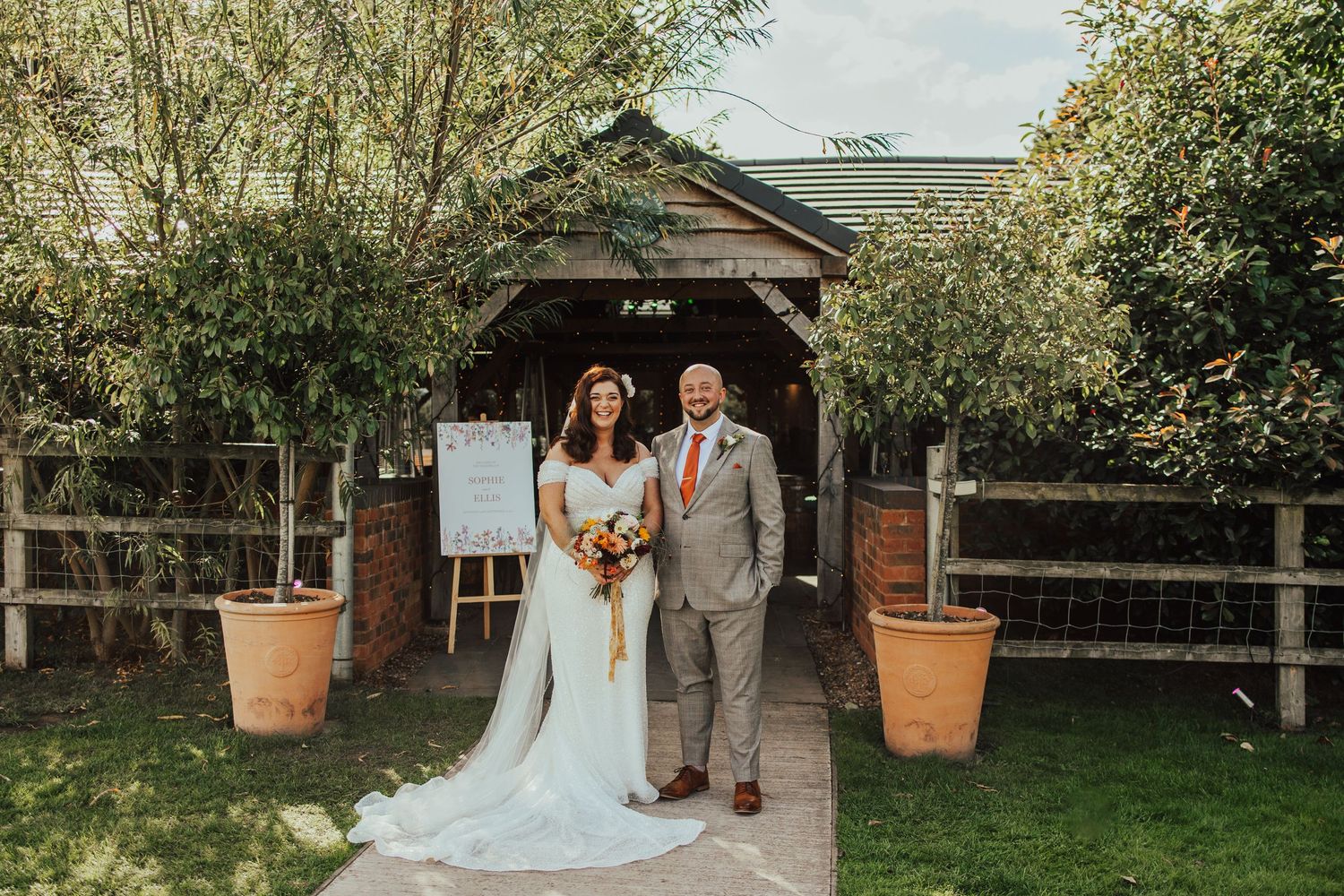 Newlywed couple walking hand in hand through scenic countryside field in formal wedding attire.