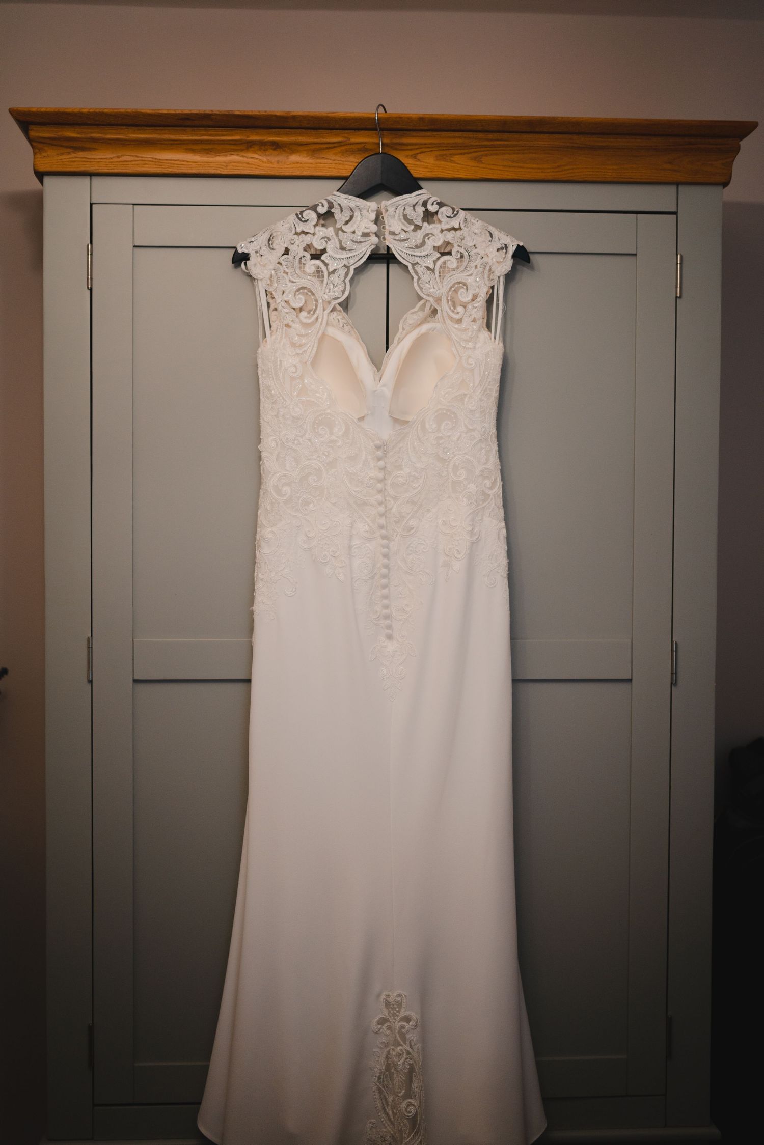 White lace wedding dress hanging on wooden beam against grey closet doors.