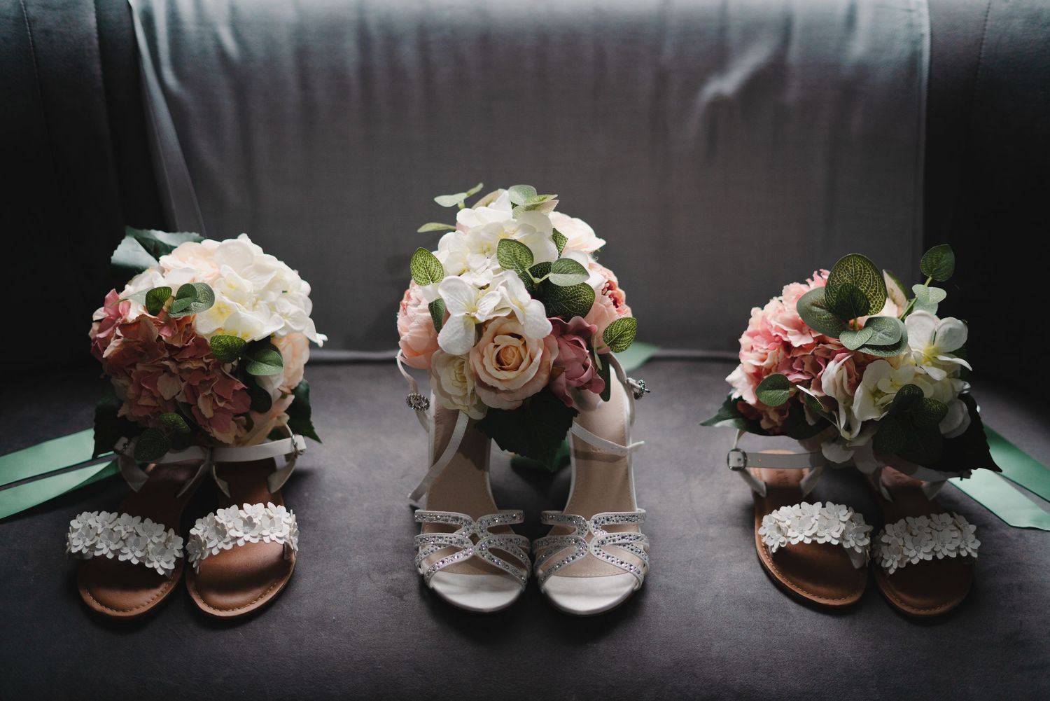 Multiple pairs of bridal shoes and accessories arranged on a dark background with soft lighting.