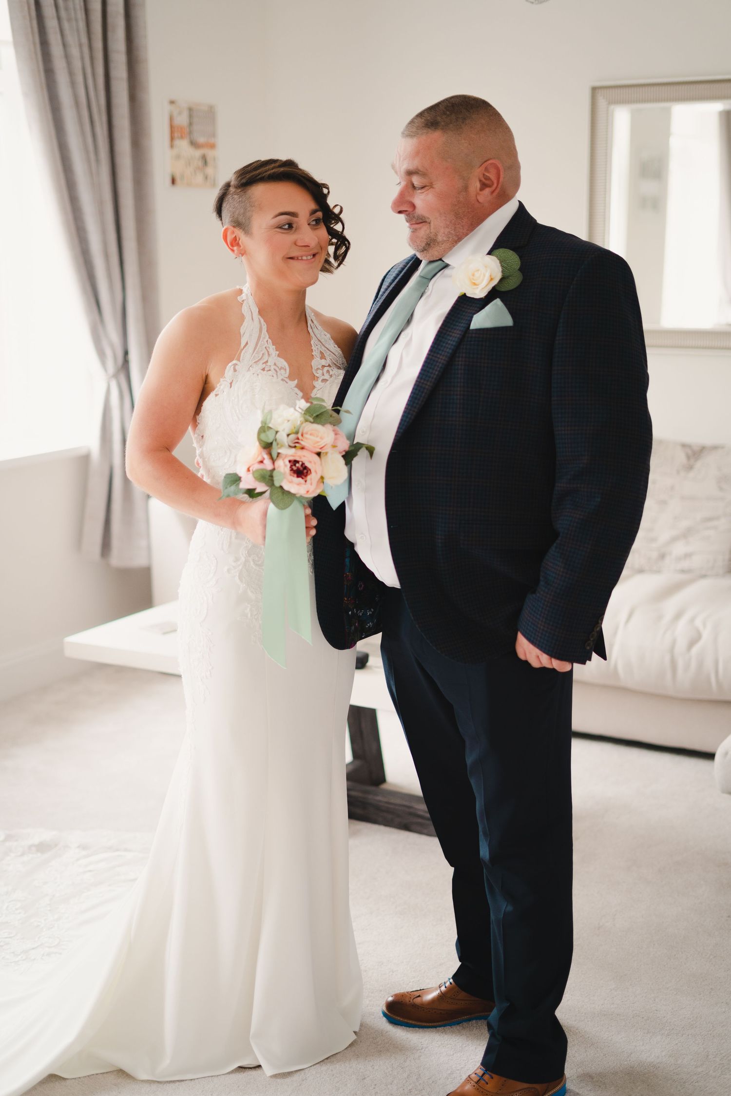 Wedding couple sharing emotional first look moment in bright sunlit room with white decor.