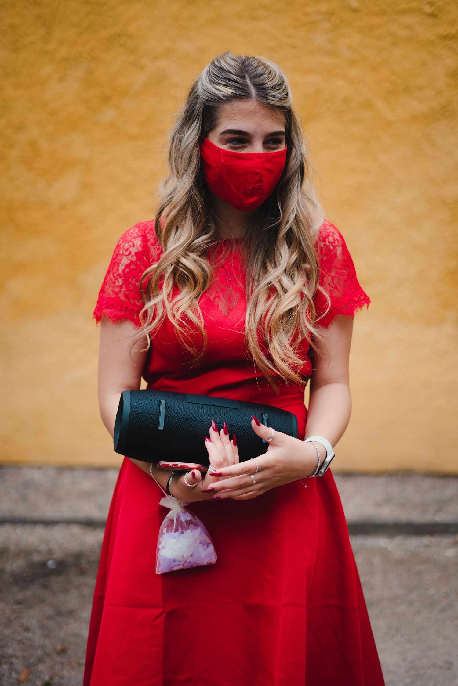 Wedding guests in red dresses wearing protective masks while holding champagne bottles.