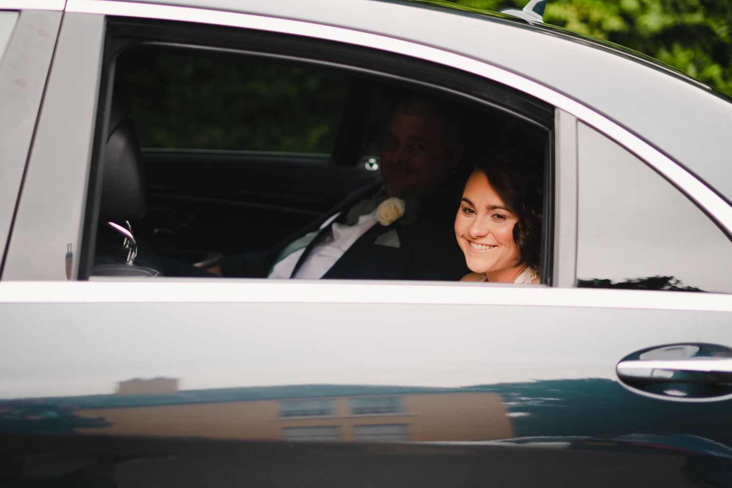 Wedding party members smiling from car windows during celebration procession.