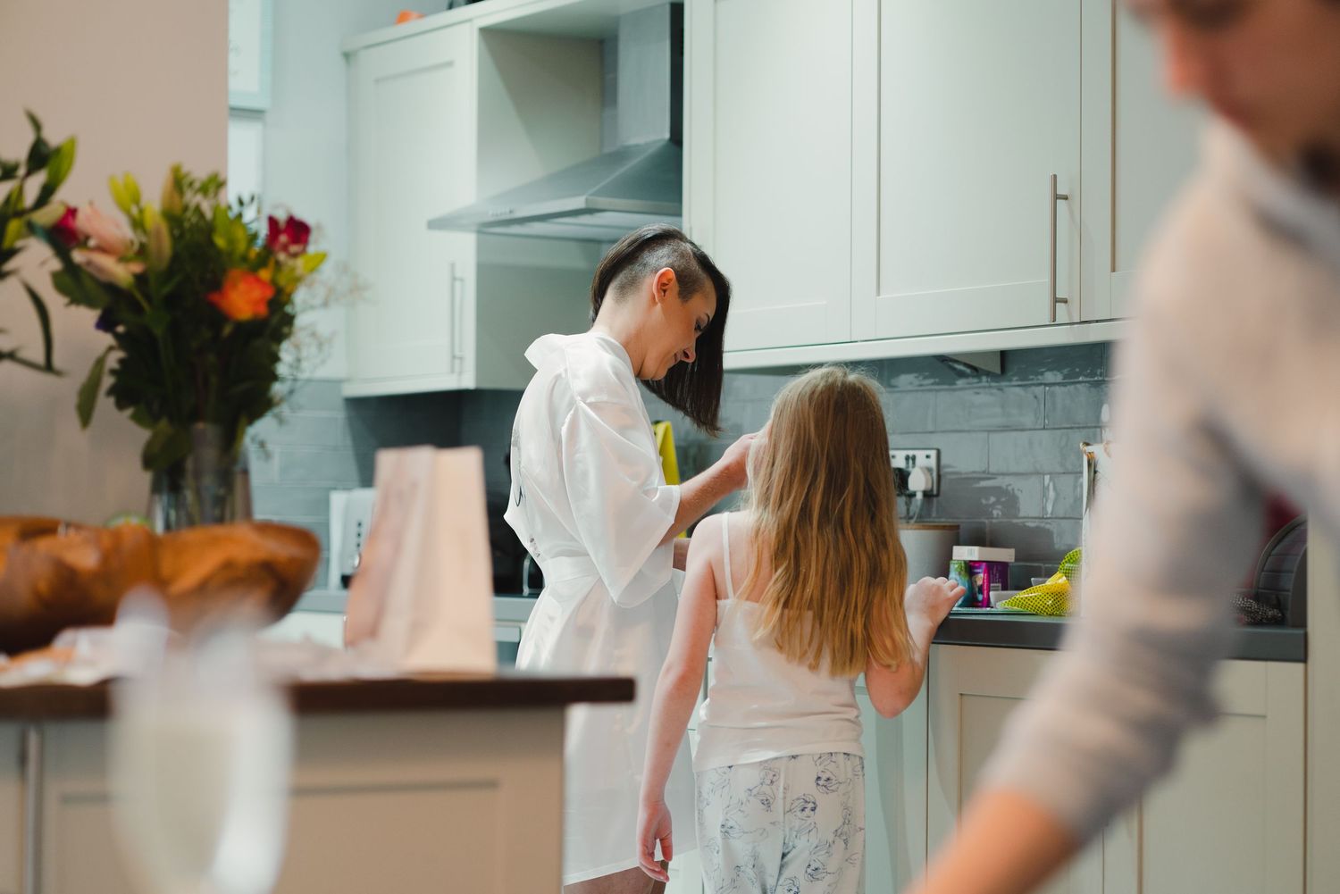 Modern white kitchen interior with people preparing food and socializing.
