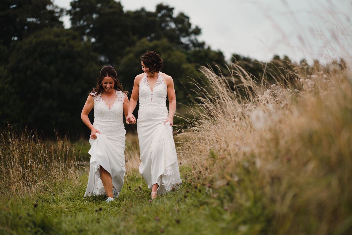 Two people in white dresses walking through a sunlit field of tall grass.
