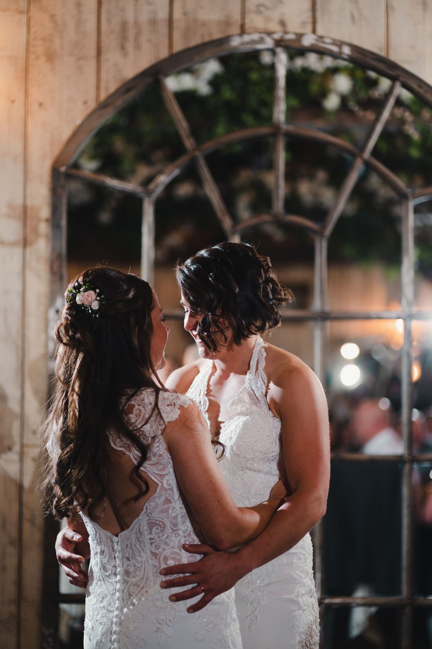 Two people in white lace dresses dancing together in a rustic wooden venue with romantic lighting.