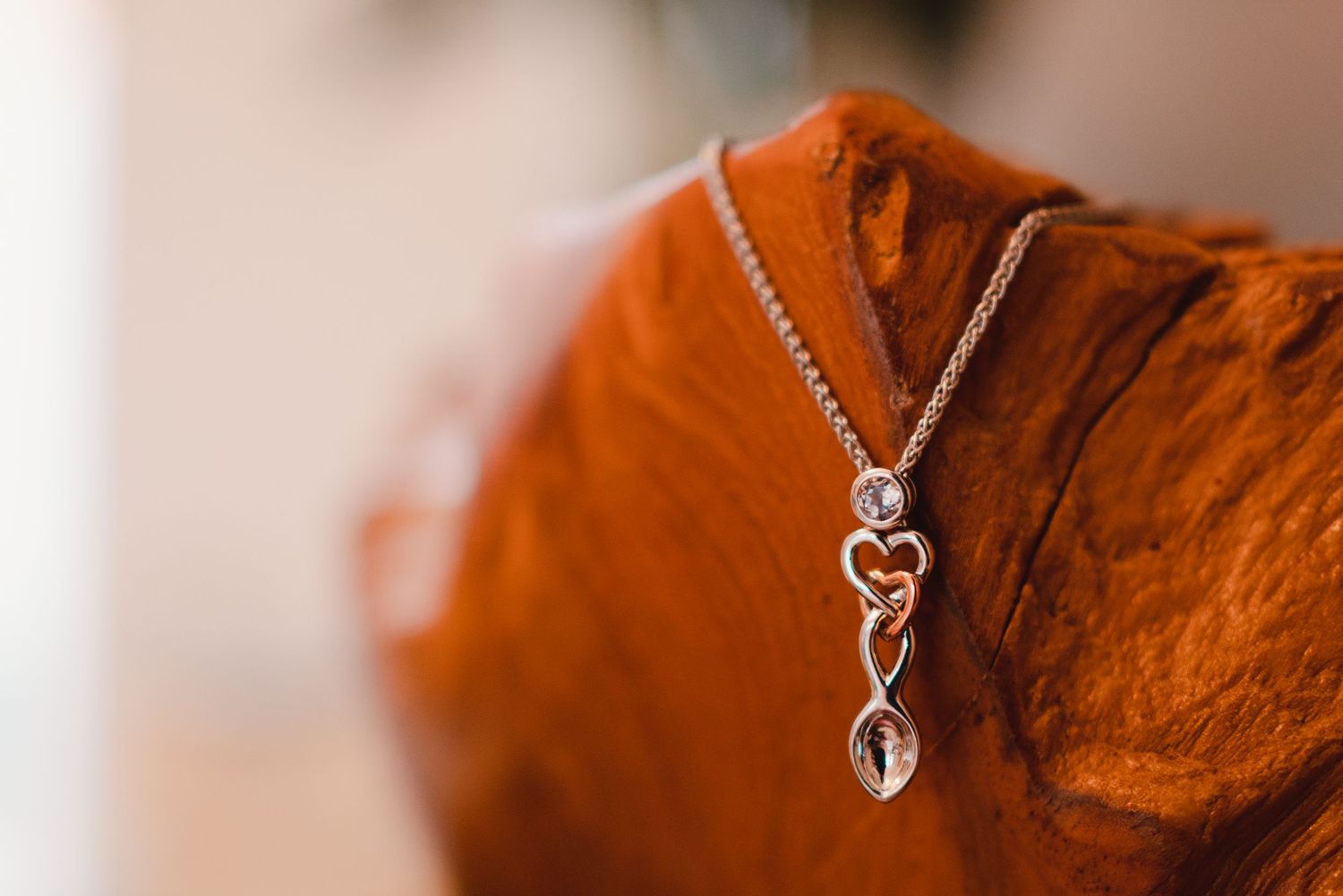 Several delicate heart-shaped pendant necklaces with silver chains displayed against a rustic reddish-brown backdrop.