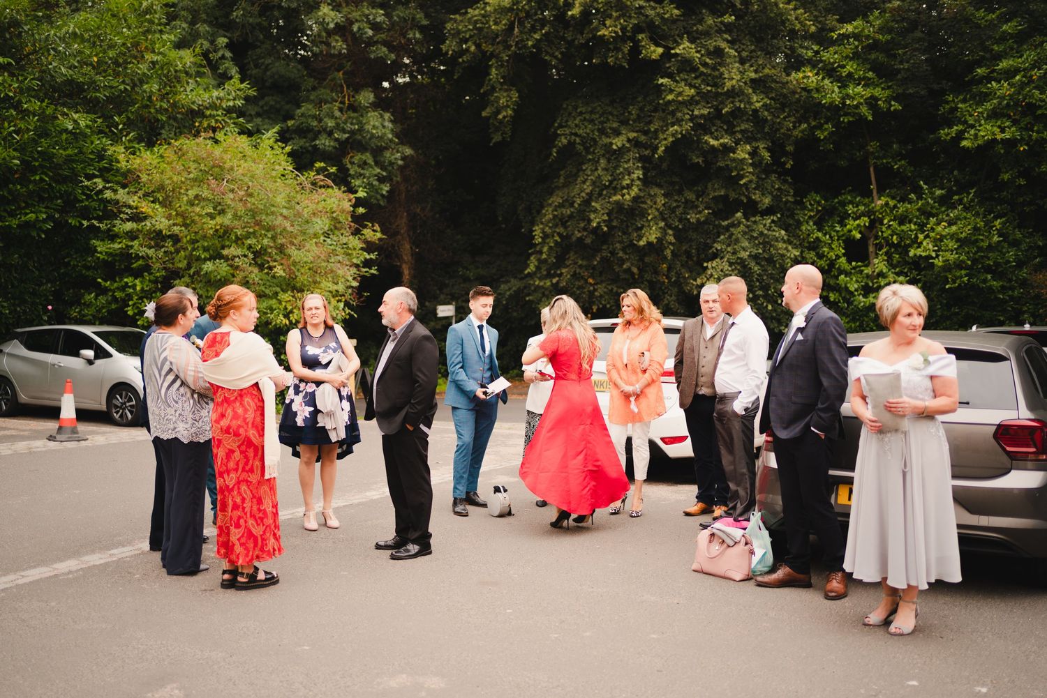 A wedding party gathered outdoors wearing formal attire with red and black color accents.