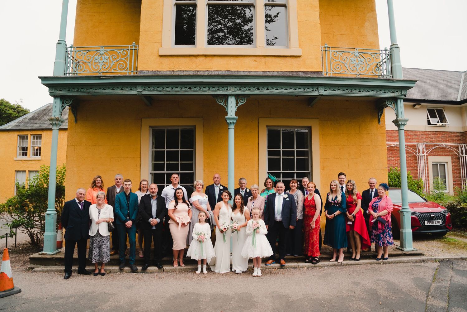 A row of yellow historic railway station buildings with wedding party groups lined up outside.
