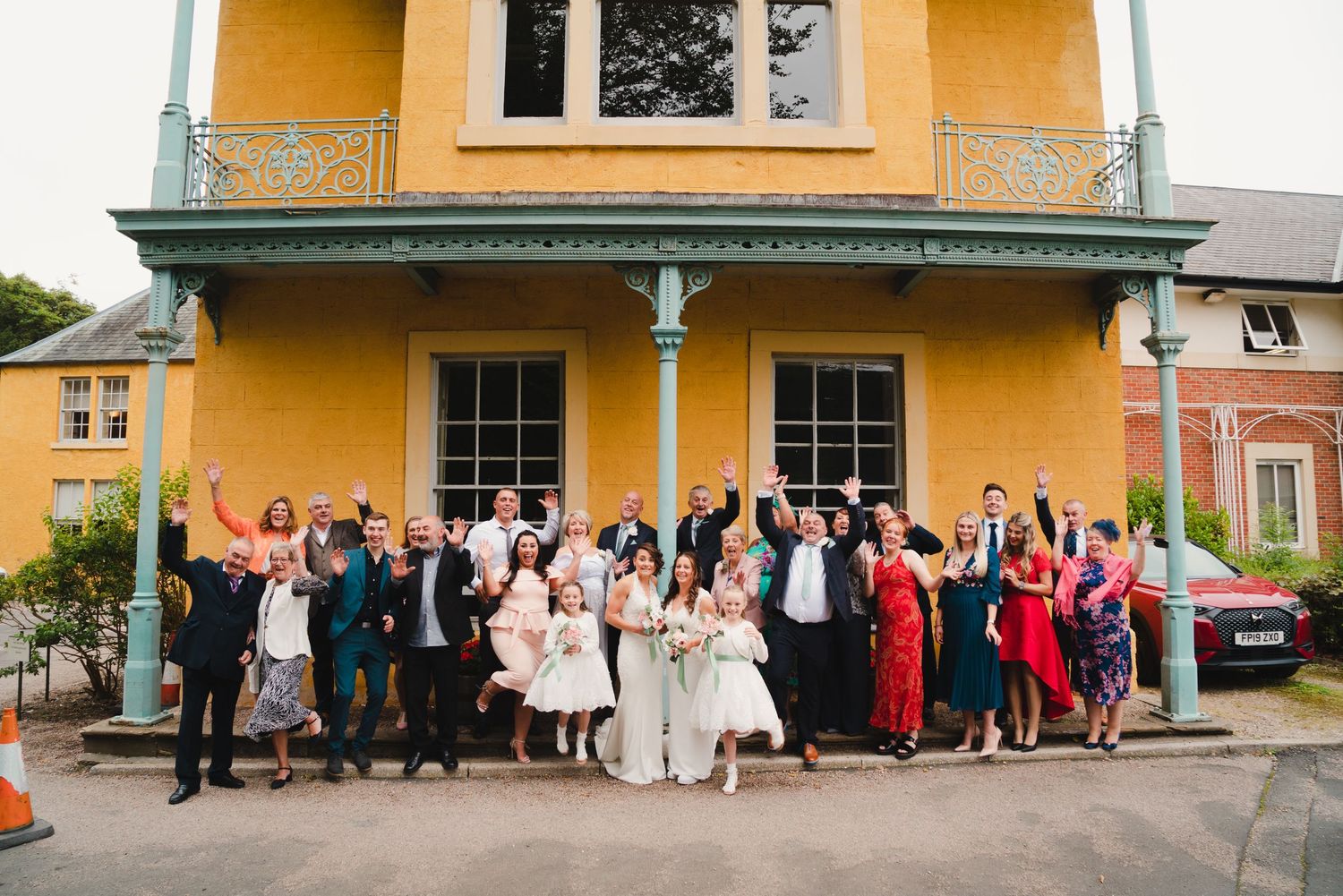 Large group gathered outside a yellow historic building for a formal event celebration in daylight.