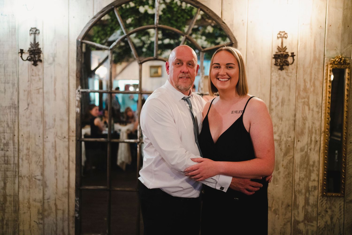 Couple posing together at an elegant venue with arched windows and wall sconces in the background.