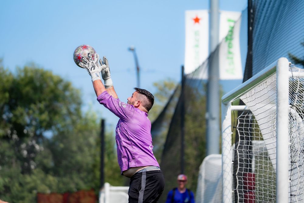 A soccer goalie in a purple jersey catches the ball before it scores in the net behind him
