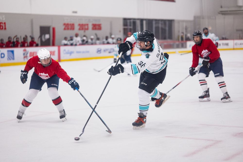 A hockey player in blue and white takes a shot on a goal offscreen, surrounded by players in red jerseys
